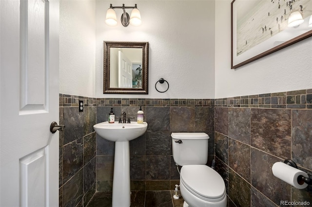 902 Jarvis Dr, Erie, CO 80516 - half bathroom featuring toilet, tile walls, a sink, and a wainscoted wall