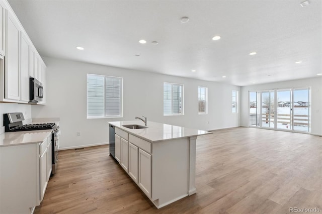 kitchen with white cabinets, stainless steel appliances, a kitchen island with sink, and light hardwood / wood-style floors