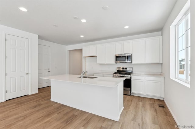 kitchen with white cabinets, an island with sink, appliances with stainless steel finishes, and light hardwood / wood-style flooring