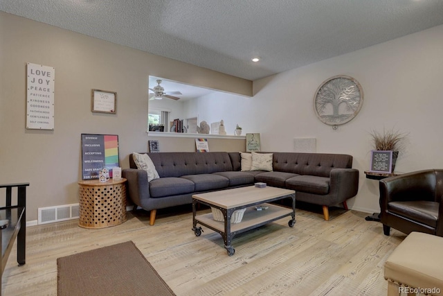 living area with baseboards, light wood-style flooring, visible vents, and a textured ceiling