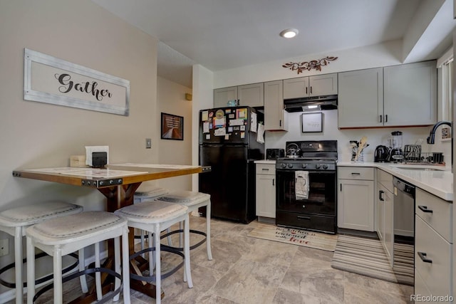 kitchen featuring a breakfast bar, light countertops, a sink, under cabinet range hood, and black appliances