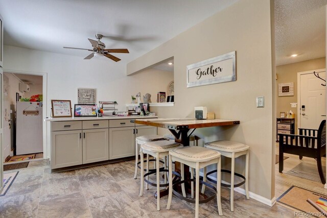 kitchen featuring baseboards, a ceiling fan, light countertops, gray cabinetry, and fridge