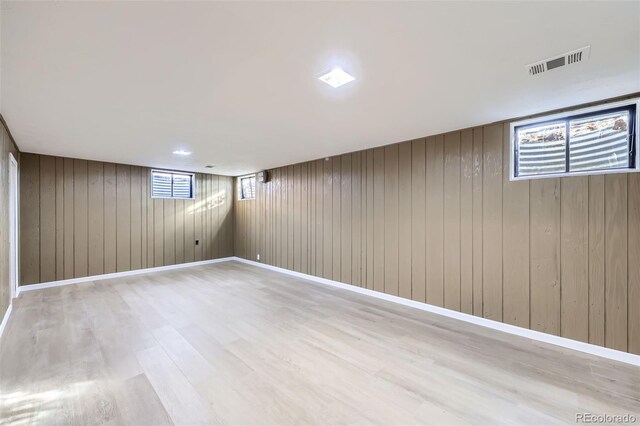 basement featuring a wealth of natural light, wood walls, and light hardwood / wood-style floors