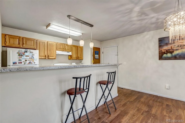 kitchen with dark wood-style floors, a kitchen breakfast bar, freestanding refrigerator, under cabinet range hood, and pendant lighting