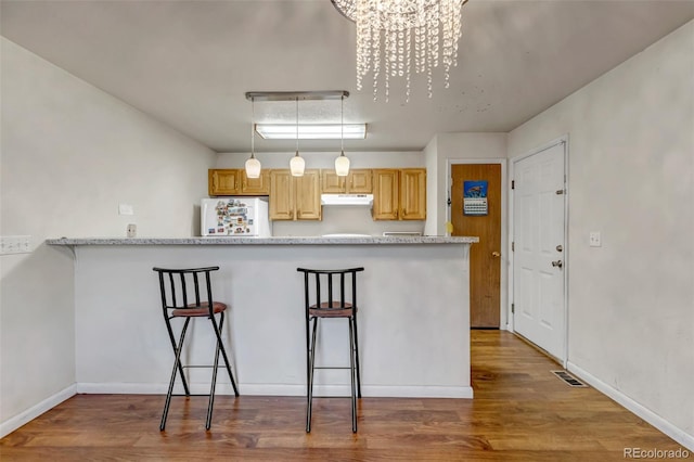 kitchen featuring a breakfast bar area, under cabinet range hood, wood finished floors, freestanding refrigerator, and decorative light fixtures