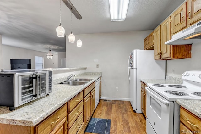 kitchen featuring light wood finished floors, light countertops, a sink, white appliances, and under cabinet range hood