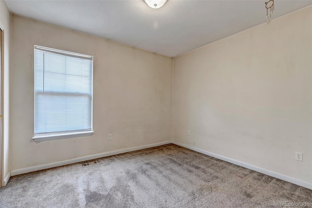 empty room with carpet, a healthy amount of sunlight, visible vents, and baseboards