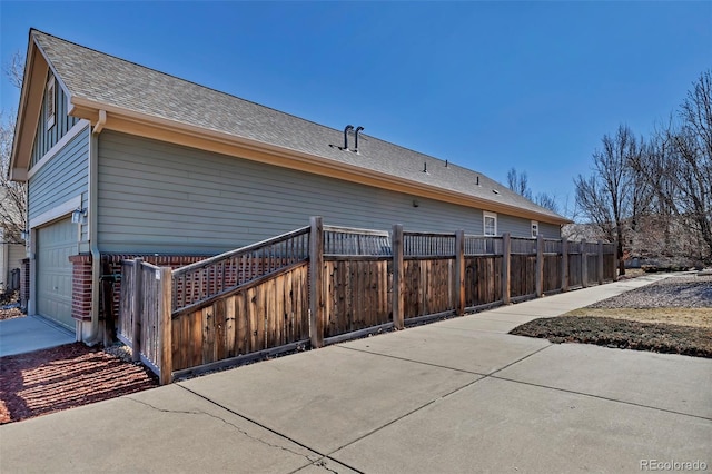 view of home's exterior with a garage, fence, and a shingled roof