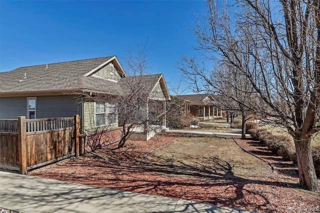 view of side of home with roof with shingles and fence