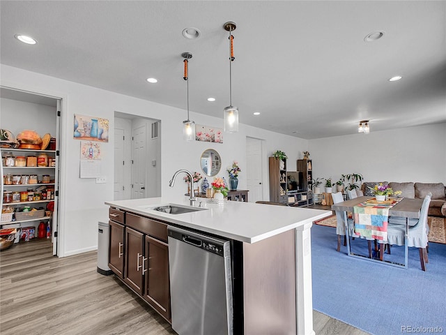 kitchen featuring light wood finished floors, open floor plan, dishwasher, light countertops, and a sink
