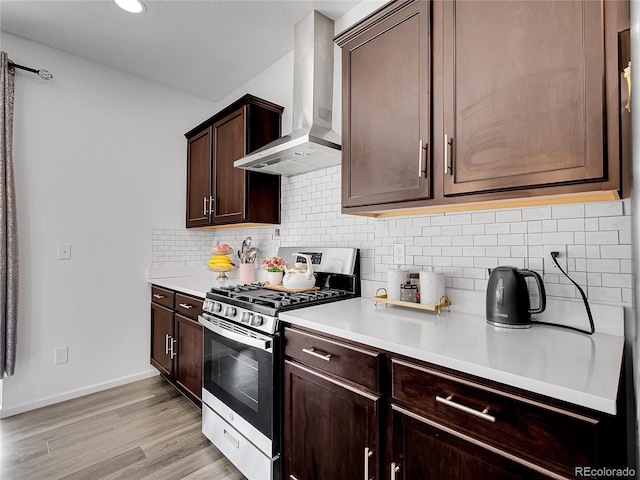 kitchen featuring light countertops, dark brown cabinetry, light wood-style floors, wall chimney range hood, and stainless steel gas stove