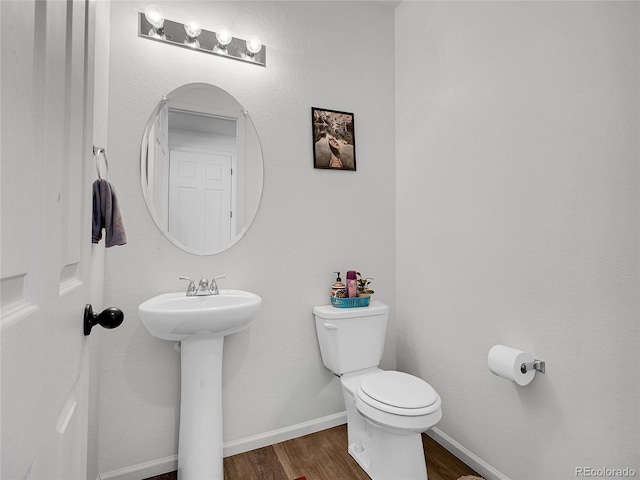 half bath with a sink, toilet, baseboards, and wood finished floors