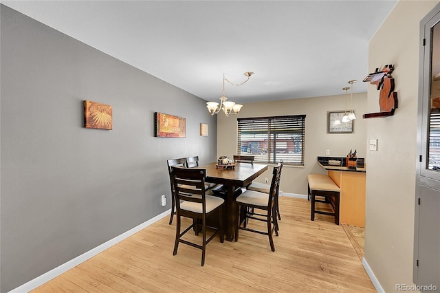 dining room with light wood-style flooring, a notable chandelier, and baseboards
