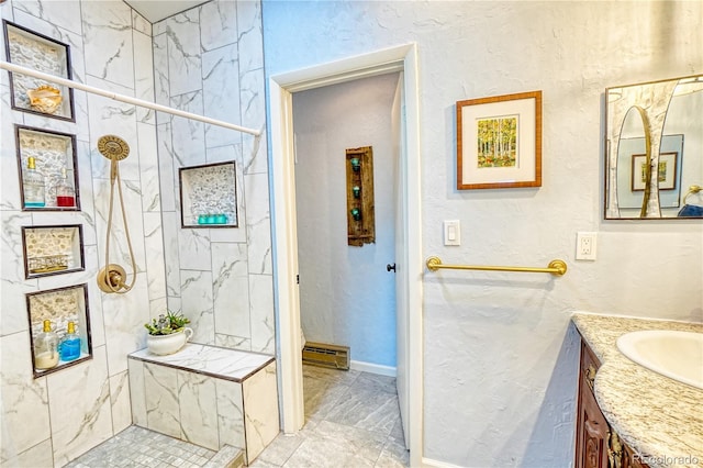 bathroom with baseboard heating, vanity, and tiled shower