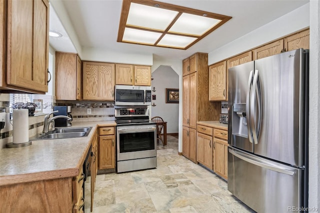 kitchen featuring light countertops, decorative backsplash, stone finish floor, stainless steel appliances, and a sink