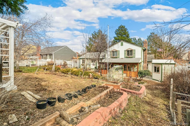 rear view of property featuring an outdoor structure, a vegetable garden, fence, and a chimney