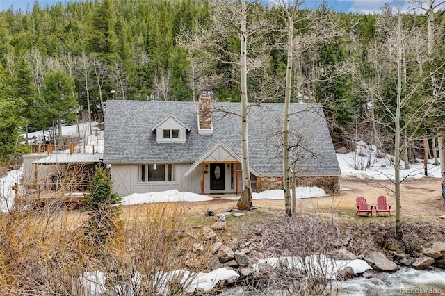 view of front facade with a chimney, board and batten siding, a forest view, and roof with shingles