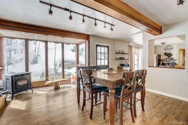 dining room featuring beam ceiling, a wood stove, rail lighting, wood-type flooring, and baseboards
