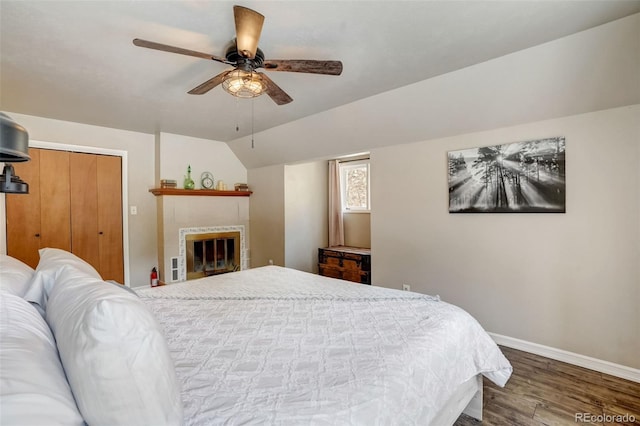 bedroom featuring lofted ceiling, wood finished floors, a fireplace, ceiling fan, and baseboards