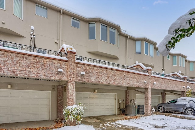 snow covered rear of property featuring a garage and central AC