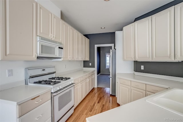 kitchen with white cabinetry, sink, white appliances, and light wood-type flooring