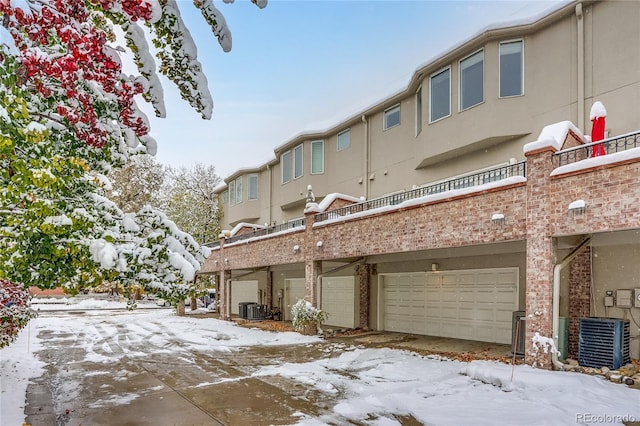 snow covered rear of property with a garage and central AC