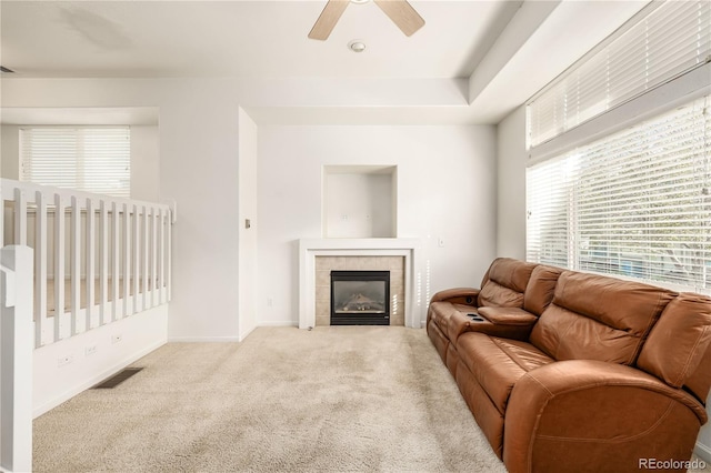 living room with a tiled fireplace, light carpet, and ceiling fan