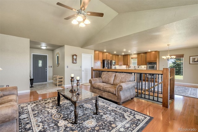 living room with a textured ceiling, high vaulted ceiling, ceiling fan with notable chandelier, and light wood-type flooring