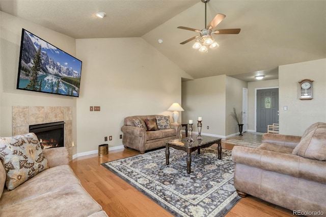 living room featuring light wood-type flooring, vaulted ceiling, a tiled fireplace, and ceiling fan