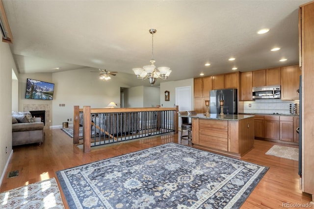 kitchen featuring a center island, light wood-type flooring, appliances with stainless steel finishes, ceiling fan with notable chandelier, and tasteful backsplash