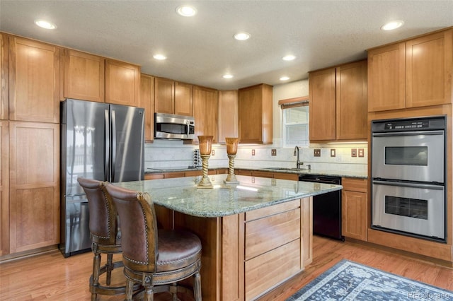 kitchen featuring appliances with stainless steel finishes, tasteful backsplash, light stone counters, light wood-type flooring, and a center island