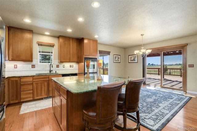 kitchen featuring light wood-type flooring, a chandelier, a kitchen island, light stone counters, and stainless steel oven