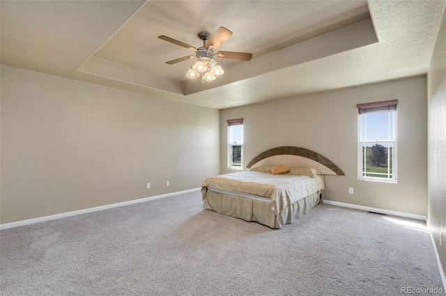 carpeted bedroom with ceiling fan and a raised ceiling