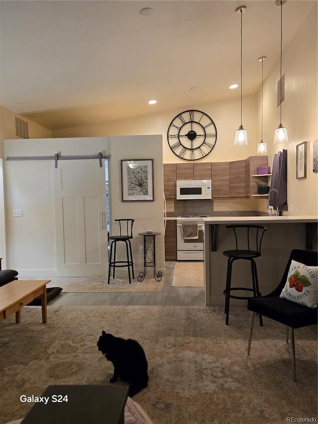 kitchen featuring a kitchen breakfast bar, a barn door, pendant lighting, white appliances, and kitchen peninsula