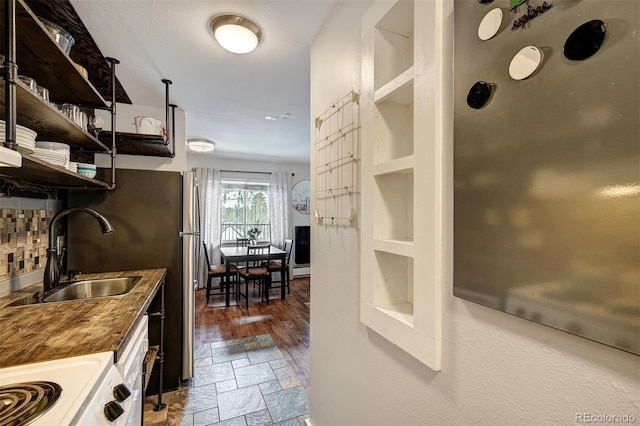 kitchen with a sink, open shelves, backsplash, stone tile floors, and stove