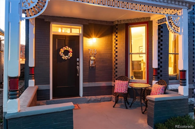 doorway to property with covered porch and brick siding