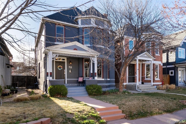victorian-style house with covered porch, brick siding, fence, and a front yard