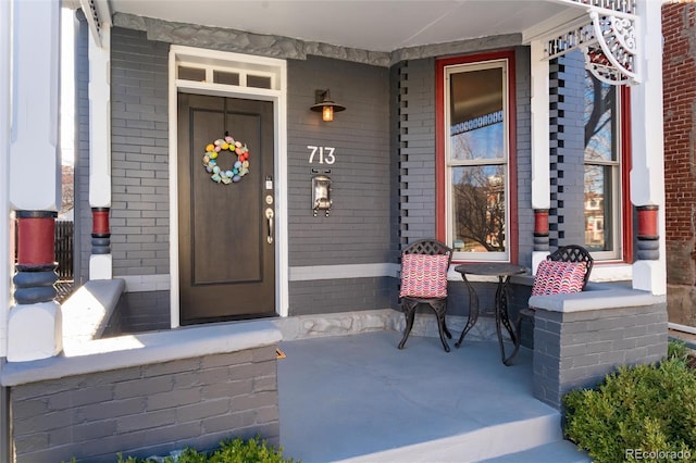 doorway to property with covered porch and brick siding