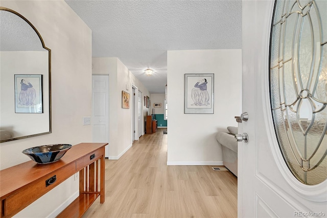 hall with light wood-type flooring and a textured ceiling