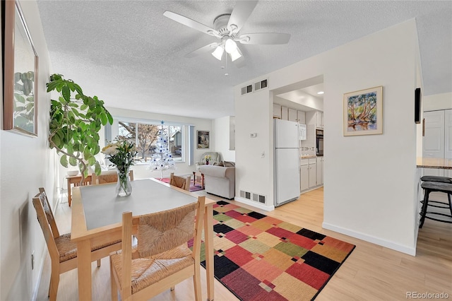 dining space with ceiling fan, light hardwood / wood-style flooring, and a textured ceiling