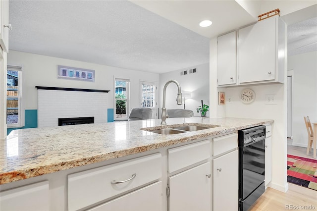 kitchen with a fireplace, black dishwasher, white cabinetry, and sink