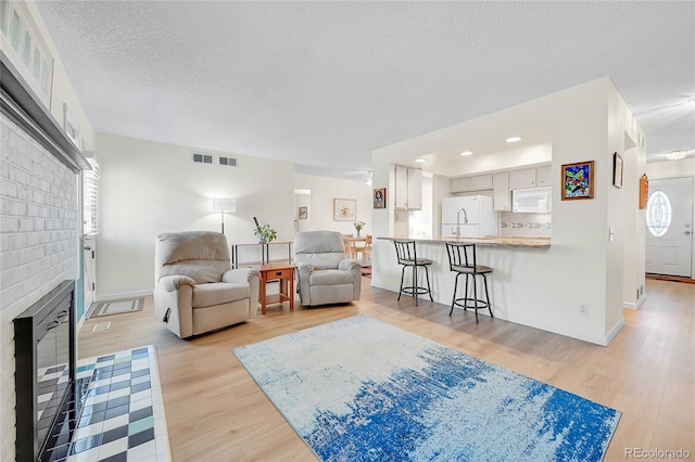 living room featuring light hardwood / wood-style floors, a textured ceiling, and a brick fireplace