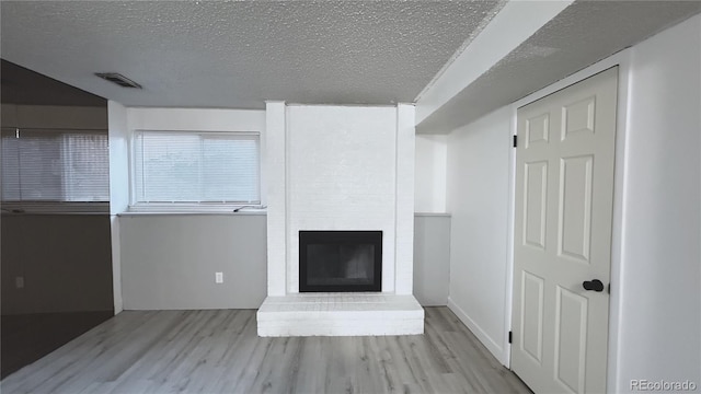 unfurnished living room featuring a brick fireplace, a textured ceiling, and light hardwood / wood-style floors