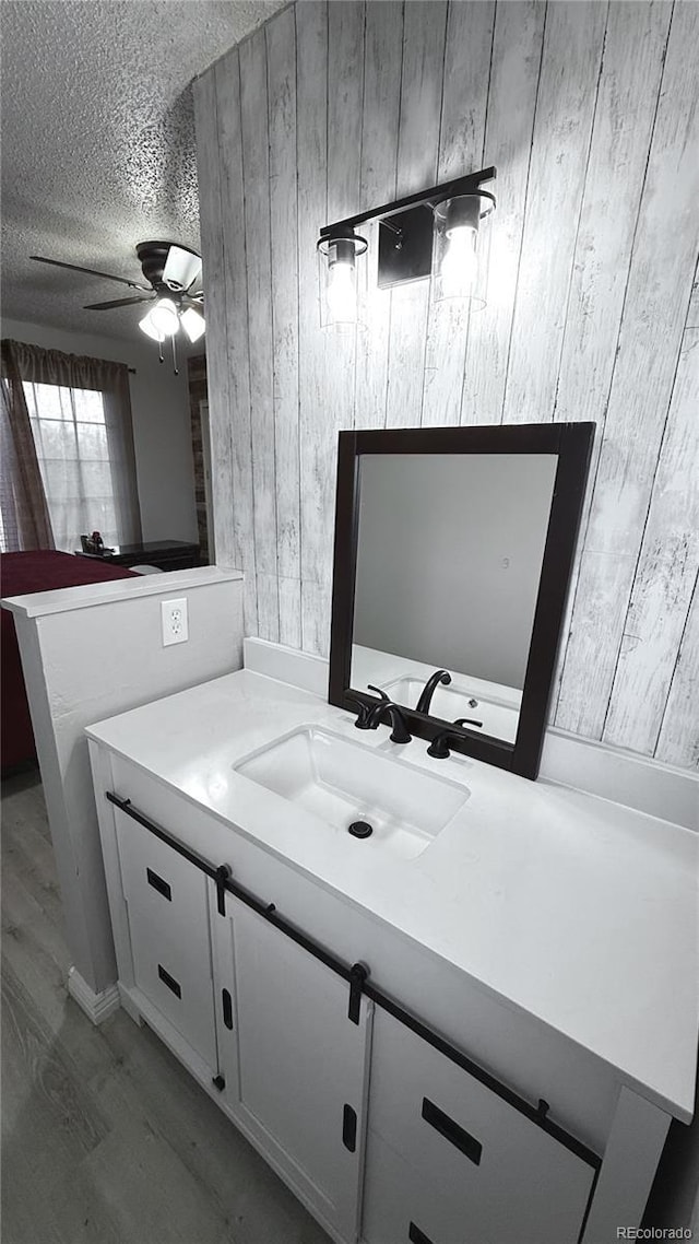 bathroom with wood walls, ceiling fan, wood-type flooring, a textured ceiling, and vanity