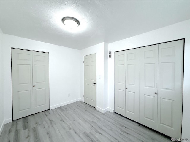 unfurnished bedroom with two closets, a textured ceiling, and light hardwood / wood-style floors