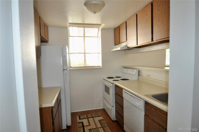 kitchen featuring white appliances, under cabinet range hood, brown cabinets, dark wood finished floors, and light countertops