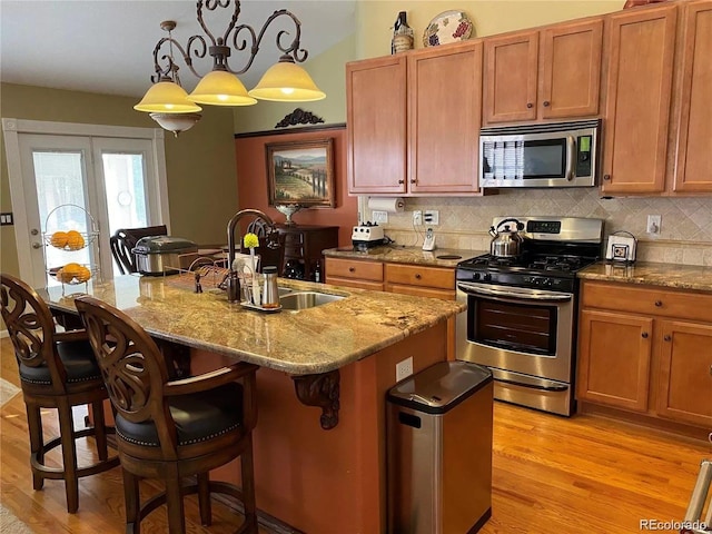 kitchen featuring sink, stainless steel appliances, a kitchen breakfast bar, decorative light fixtures, and a center island with sink