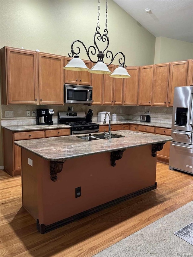 kitchen featuring stainless steel appliances, vaulted ceiling, a kitchen island with sink, and light hardwood / wood-style flooring