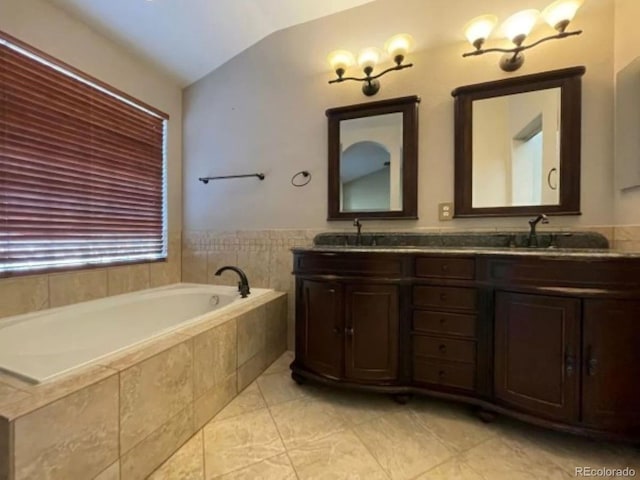 bathroom featuring tiled bath, vanity, and vaulted ceiling