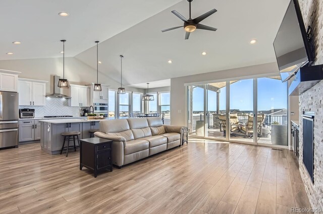 living room featuring lofted ceiling, a stone fireplace, sink, ceiling fan, and light hardwood / wood-style flooring